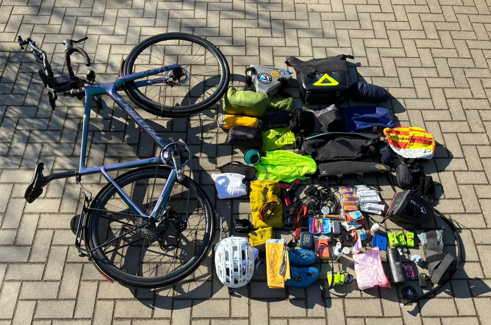 Flatlay des kompletten Ultra-Distanz-Setups mit Rad und ausgelegtem Material auf Pflastersteinen.